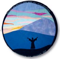 Quilt depicting St. Francis with arms raised, mountains with sunlight behind in the background